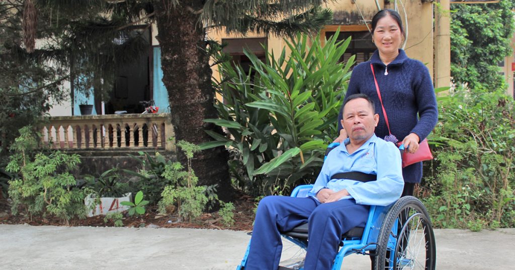 In Vietnam, a woman pushes her husband in a wheelchair after he lost mobility to a stroke.