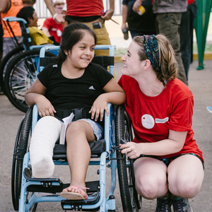 A volunteer kneels next to a young girl in a wheelchair, in Peru.