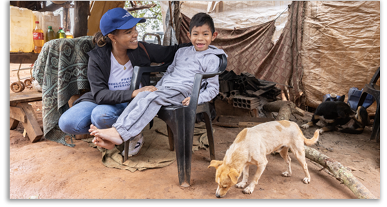 A woman meets a seven-year-old indigenous boy in Brazil, who is sitting in front of his home with his dog. 