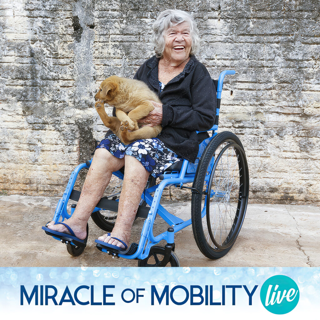 A happy looking older woman in a new blue wheelchair, with her dog in her lap.