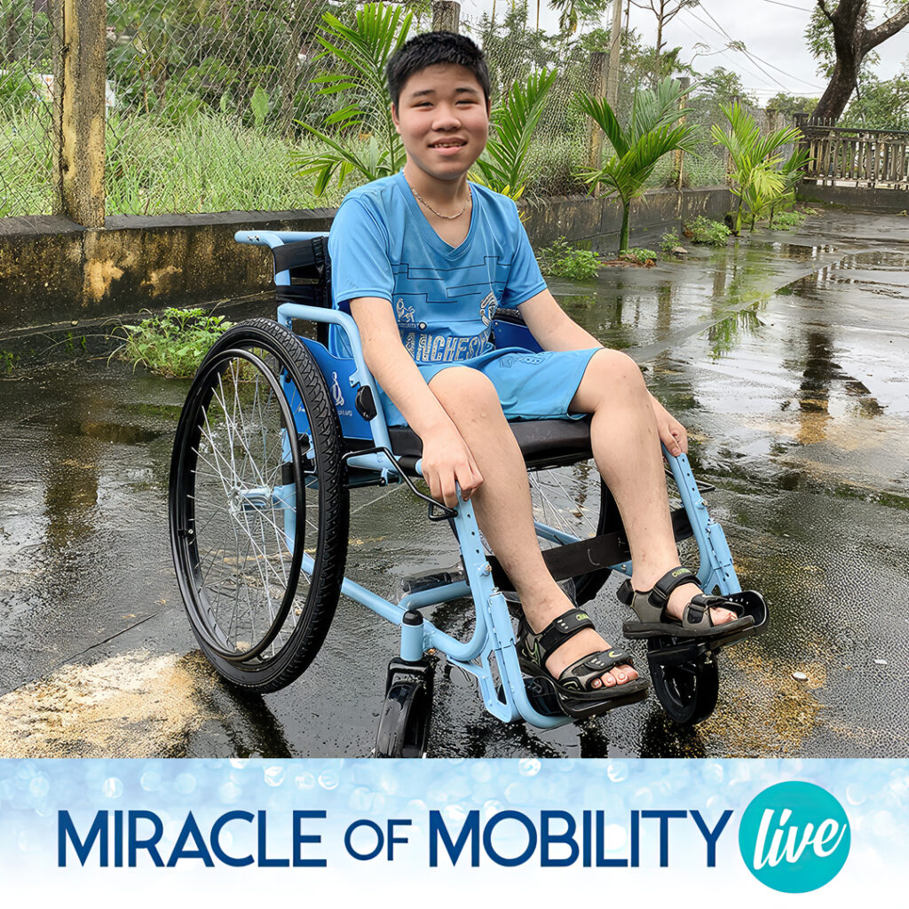 A teenaged boy in Vietnam smiles as he sits in his new blue wheelchair.