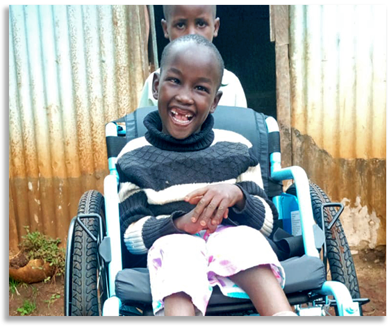 A grinning boy named Ian in Kenya, sitting in a wheelchair being pushed by his brother.