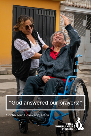 A Peruvian man raises one hand to the sky while sitting in a wheelchair, with his wife standing nearby.